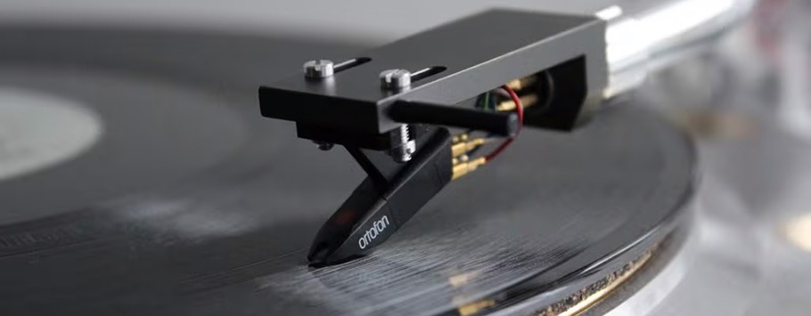 Close-up of a stylus needle on a spinning vinyl record with a tonearm. The tone is nostalgic, evoking a sense of classic music appreciation.